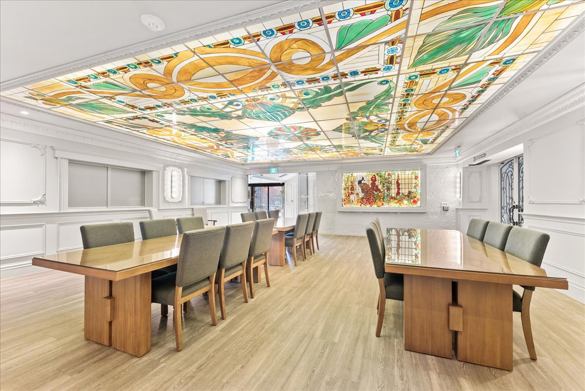 A dining room at Rodman Hall with long shared tables beneath a stained-glass ceiling