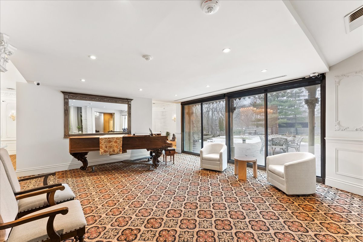 A bright room at Rodman Hall with a grand piano and armchairs looking onto the terrace